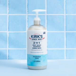 A bottle of Fragrance Free - 3-in-1 Cleanser with a pump is placed against a backdrop of blue tiles. The label highlights that it is a fragrance free body wash, shampoo, and bubble bath made with coconut oil, suitable for sensitive skin.